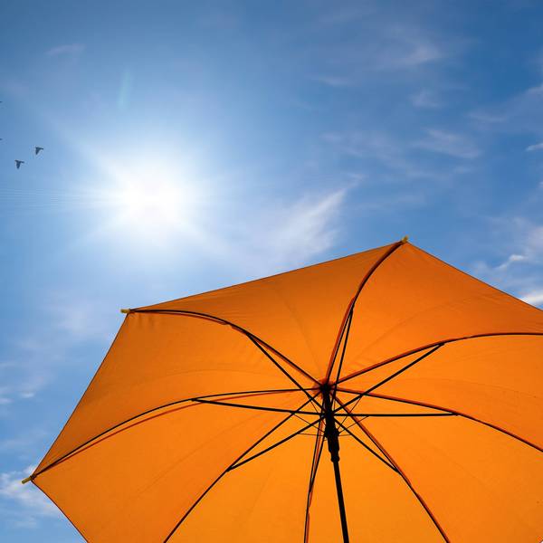 blauer Himmel, oranger Sonnenschirm, strahlende Sonne