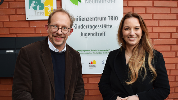 Oberbürgermeister Tobias Bergmann und Innenministerin Magdalena Finke stehen vor dem enthüllten Schild des Familienzentrums Trio.