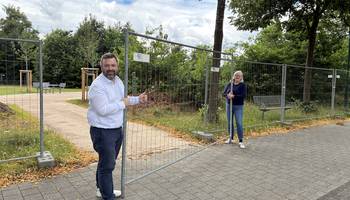 Stadtteilvorsteher Adrian Jendritzki und Stadtbaurätin Sabine Kling heben den Bauzaun beiseite: Die Mehrgenerationenwiese in Ruthenberg ist für die Nutzung freigegeben.