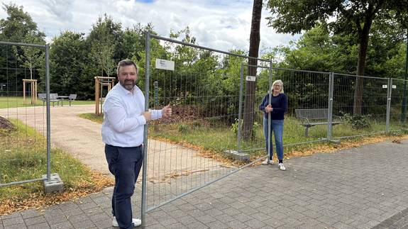 Stadtteilvorsteher Adrian Jendritzki und Stadtbaurätin Sabine Kling heben den Bauzaun beiseite: Die Mehrgenerationenwiese in Ruthenberg ist für die Nutzung freigegeben.