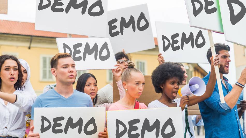 Demonstranten halten Schilder mit der Aufschrift „Demo“ nach oben.