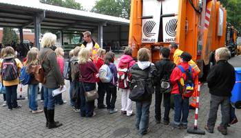 Schülerinnen und Schüler lassen sich erklären, wie ein Müllfahrzeug funktioniert. 