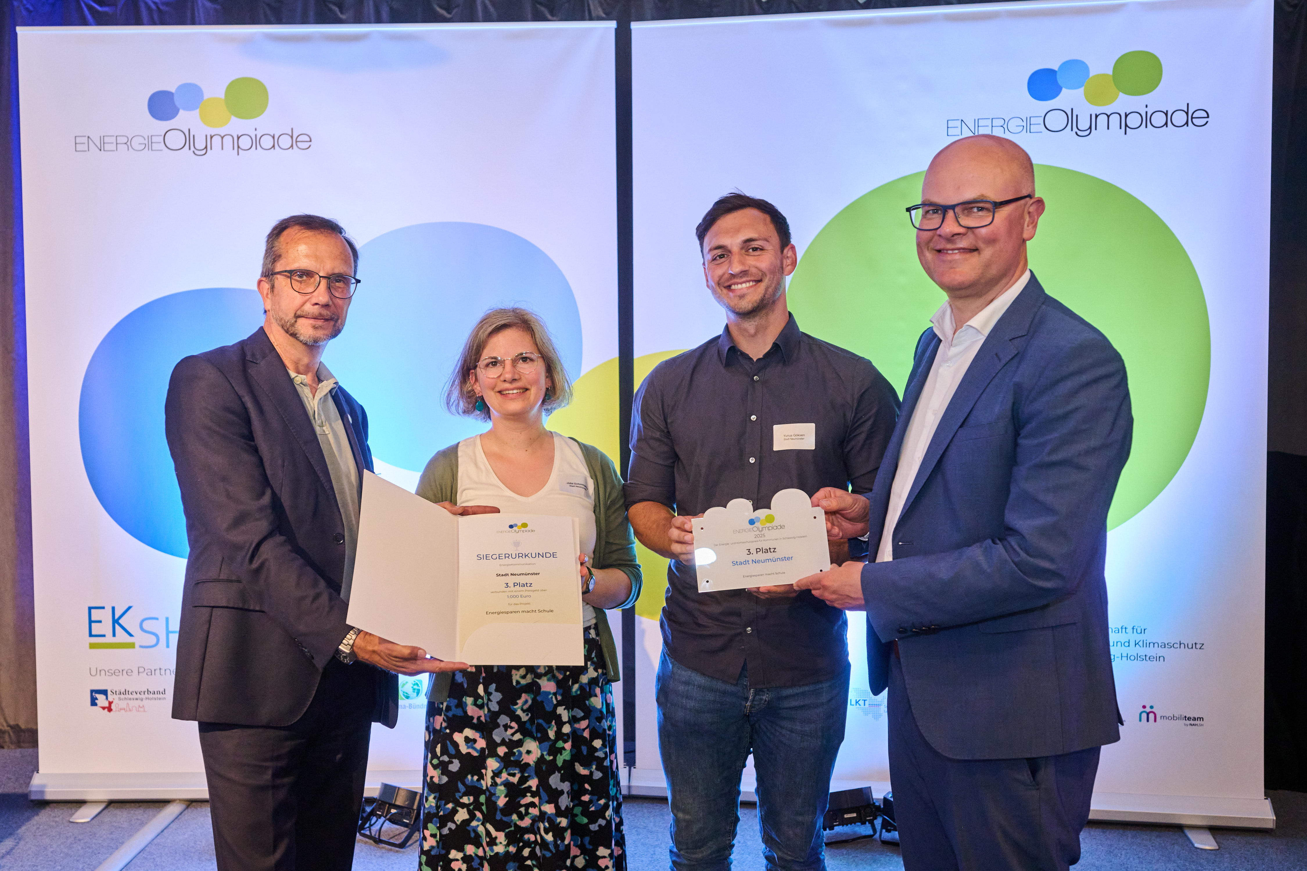Prof. Dr. Frank Osterwald (EKSH), Julia Schirrmacher & Yunus Göksen (Stabsstelle Klima & Umweltqualität, Stadt Neumünster), Tobias Goldschmidt (Klimaschutzminister, Schleswig-Holstein) bei der Überreichung der Auszeichnung